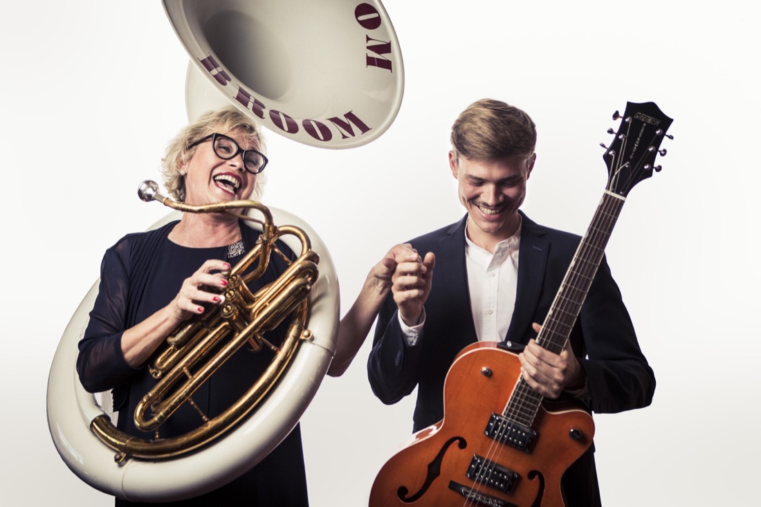 Heike lacht am Sousaphon, Julius steht mit Gitarre daneben. Auf dem Schalltrichter steht BOOM BOOM BROOM.